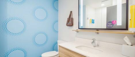 A bathroom with a blue wall, a white toilet, a wooden vanity, a mirror, and a towel rack.