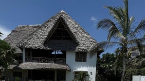 Ein Haus mit Strohdach, Swimmingpool und einem Garten mit Palmen.
