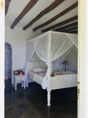 A four-poster canopy bed with white bedding and a small bedside table with a lamp.