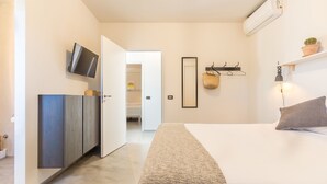Een moderne slaapkamer met een bed, een aan de muur bevestigde televisie, een spiegel en een plankje met een plant.