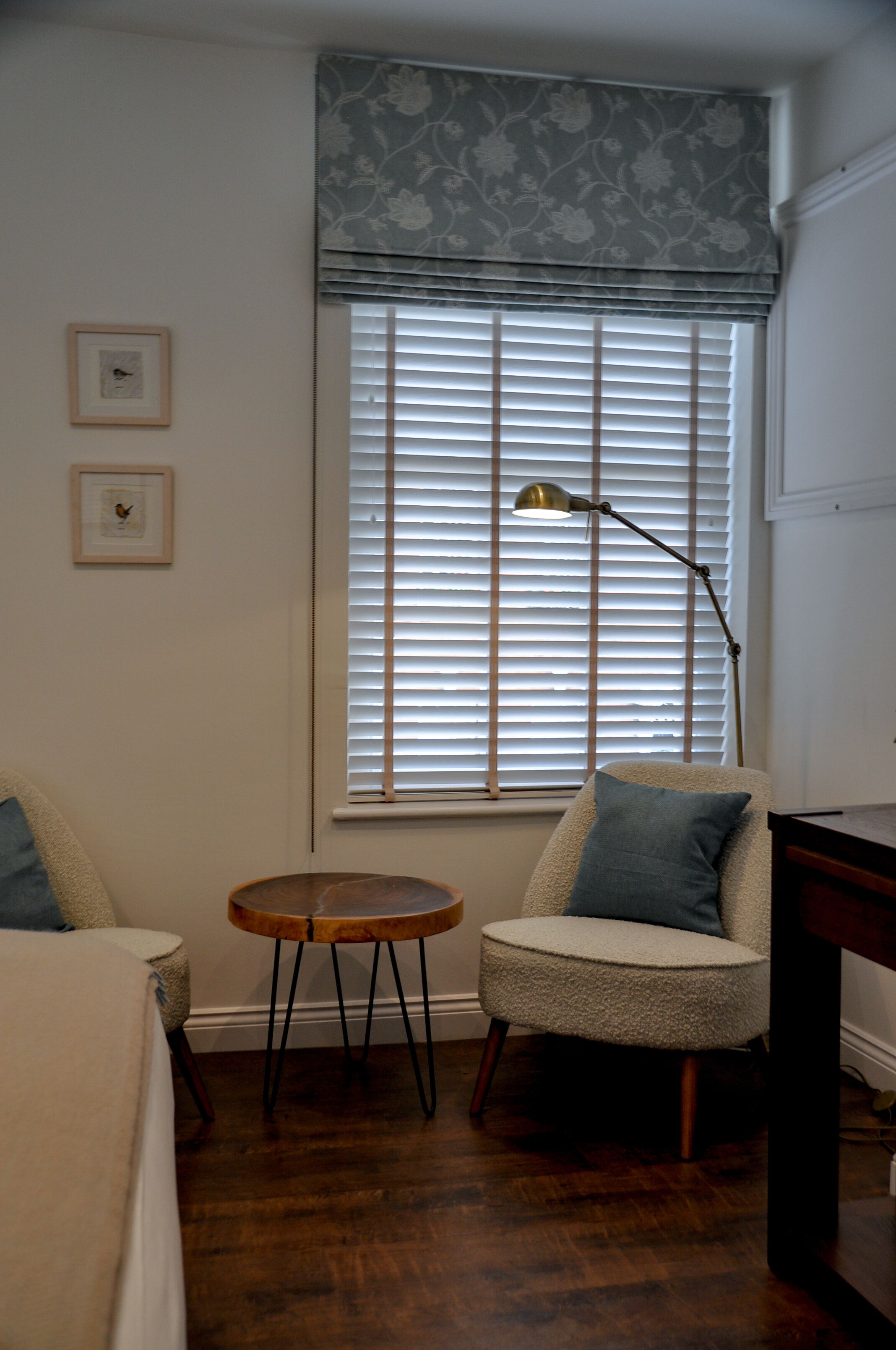 Una habitación con ventana con persianas, una lámpara de pie, una mesita redonda y dos sillas.