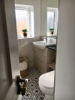 Un baño con un lavabo blanco, un inodoro y una ventana con plantas en macetas.
