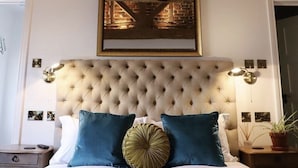 A bedroom with a tufted headboard, a framed picture above the bed, and a bedside table with a lamp. - Upstairs at 33 (Worcester)