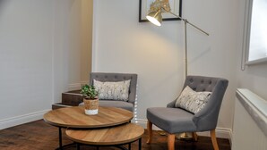 A room with a round wooden table, two grey upholstered chairs, a floor lamp, and a framed picture on the wall. - Upstairs at 33 (Worcester)
