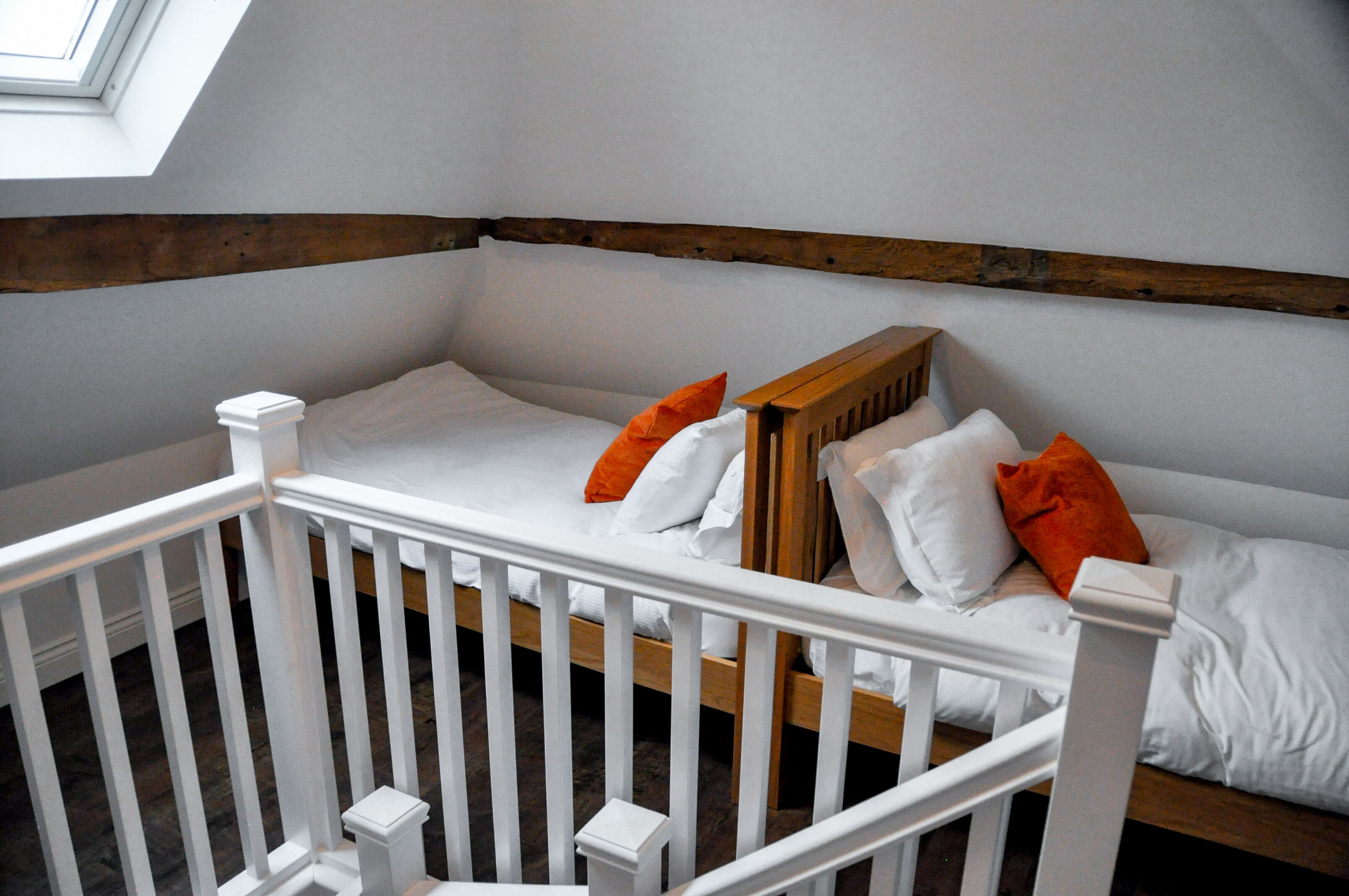A white crib with wooden headboard, white bedding, and orange pillows.