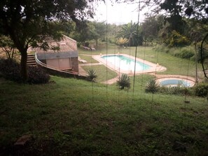 A backyard with a swimming pool, a small deck, and a grassy area with plants. - Mwingi Cottage Hotel (Mwingi)