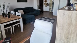 A modern living room with a sofa, a dining table with chairs, a white armchair, and a wooden coffee table. There is a painting on the wall and a hanging light fixture. - BEAUTIFUL APARTMENT ON THE SEA OF THE SEA. (moya)