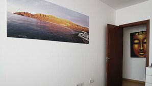 A bedroom with a bed, a wall-mounted painting of a landscape, a door, and a small white dresser. - BEAUTIFUL APARTMENT ON THE SEA OF THE SEA. (moya)