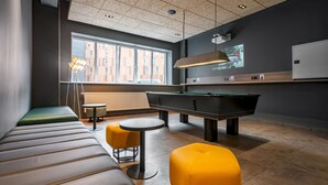 A modern lounge area with a pool table, seating, and a large window providing a view of the city. - a&o Copenhagen Sydhavn - Hostel (Copenhagen)