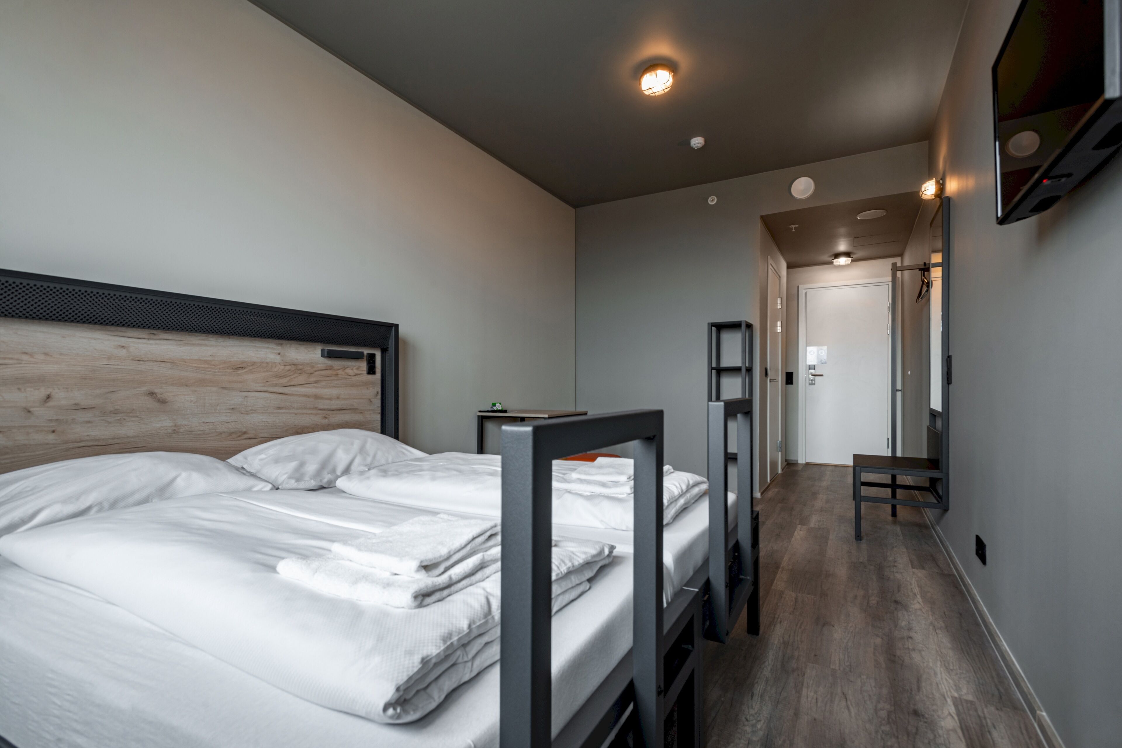 Una habitación de hotel moderna con una cama grande, un cabecero de madera y una mesita pequeña.