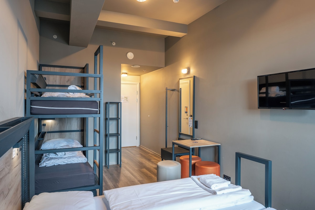 Una habitación de hotel compacta con literas, un escritorio, una silla, un espejo y una televisión.