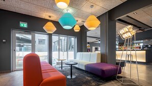 A modern lobby with colorful seating, a reception desk, and large windows allowing natural light. - a&o Copenhagen Sydhavn - Hostel (Copenhagen)