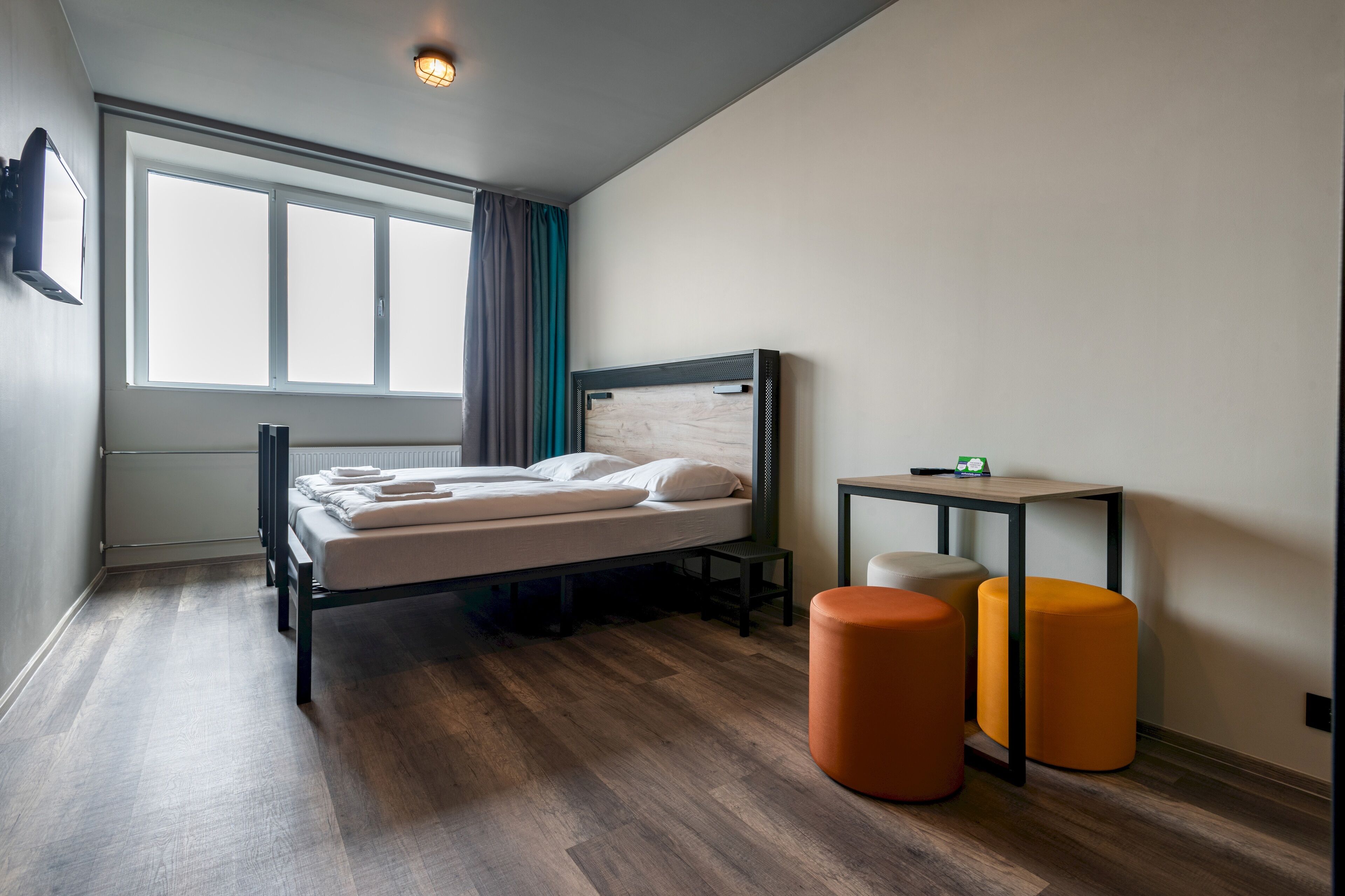 A modern bedroom with a bed, a nightstand, a small table, and two ottomans.