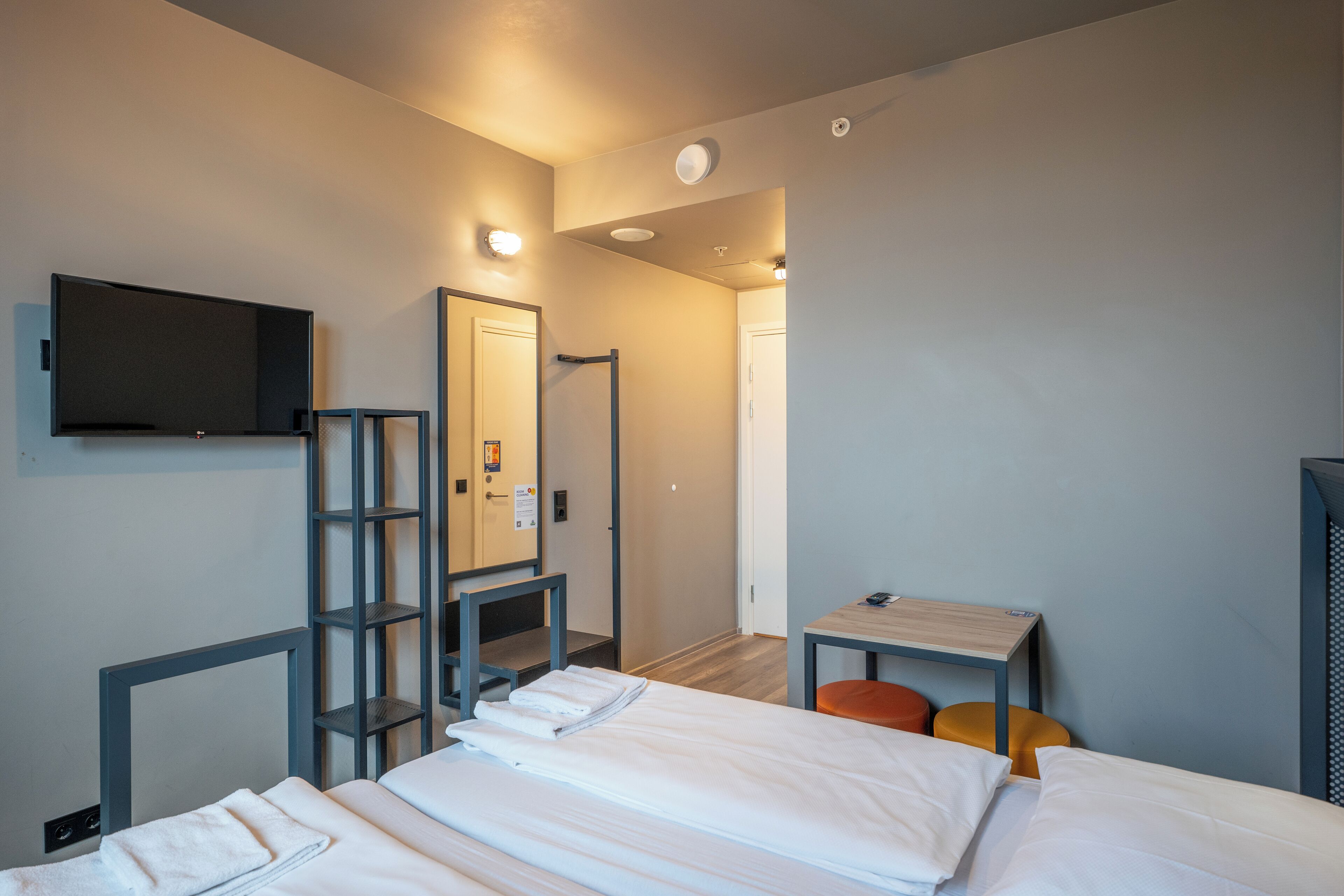A hotel room with a bed, a desk, a chair, a TV mounted on the wall, and a bathroom visible through an open door.