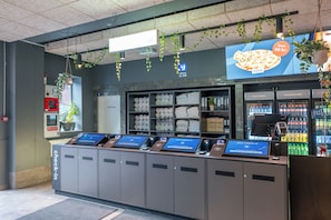 A self-check-in kiosk with multiple screens, a vending machine, and a display of bottled water. - a&o Copenhagen Sydhavn - Hostel (Copenhagen)