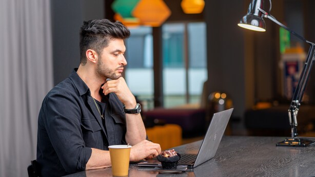 A person sitting at a table with a laptop, a coffee cup, and a desk lamp. - a&o Copenhagen Sydhavn - Hostel (Copenhagen)