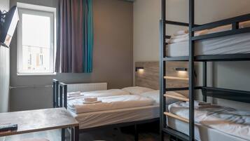 A dormitory room with bunk beds, a table, and a window with curtains.