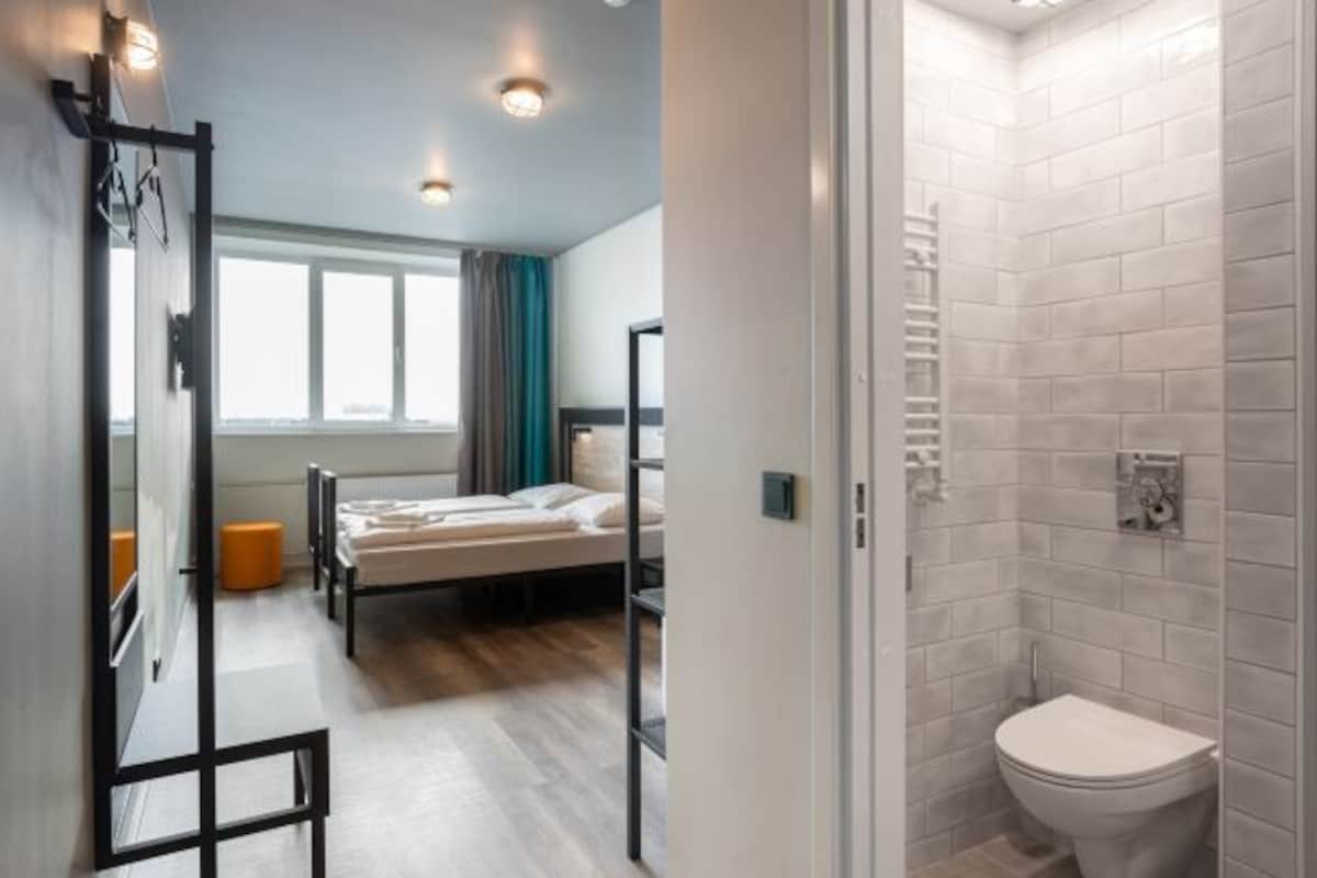 Una habitación de hotel moderna con cama, ventana y baño completo.