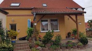 Ett tvåvåningshus med ett tak täckt av tegelpannor, en veranda med krukväxter och en fasad av tegel.