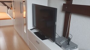 Ett modernt sovrum med en säng, en tv på ett vitt skåp och en värmare på golvet.