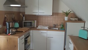 Ett kompakt kök med vita skåp, en mikrovågsugn, en spis och ett handfat.