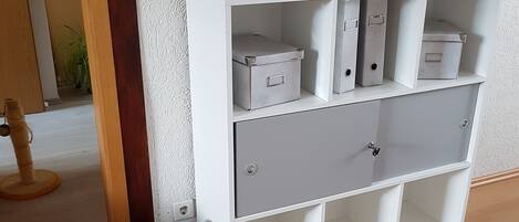 Een witte bergingsunit met verschillende vakken, een potplant en een prullenbak.