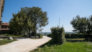 A rural road with a building on the left, surrounded by trees and greenery. - GFH - Hotel Palazzo Bello (Recanati)
