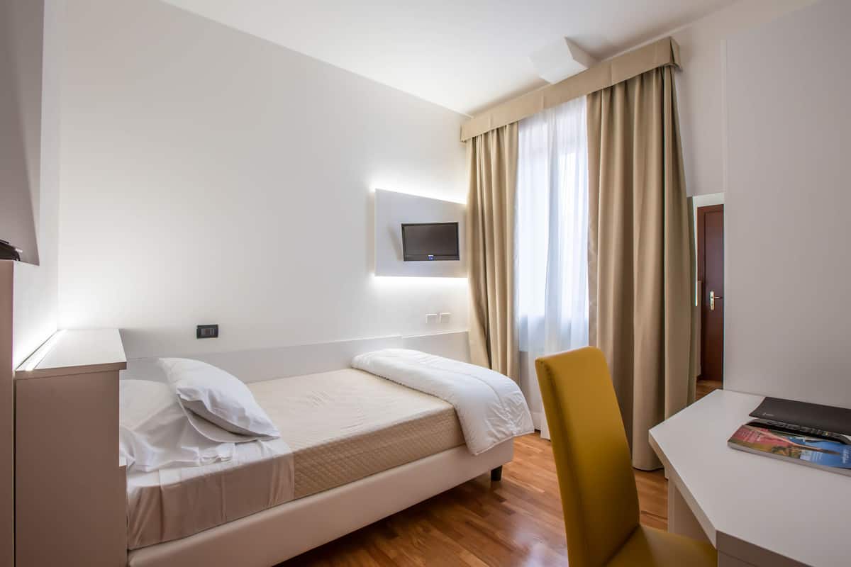 Une chambre d’hôtel équipée d’un lit, d’un bureau, d’une chaise, d’un téléviseur fixé au mur et d’une fenêtre avec des rideaux.