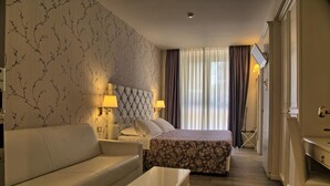 A hotel room with a bed, a sofa, a coffee table, and a desk with a lamp. - GFH - Hotel Palazzo Bello (Recanati)
