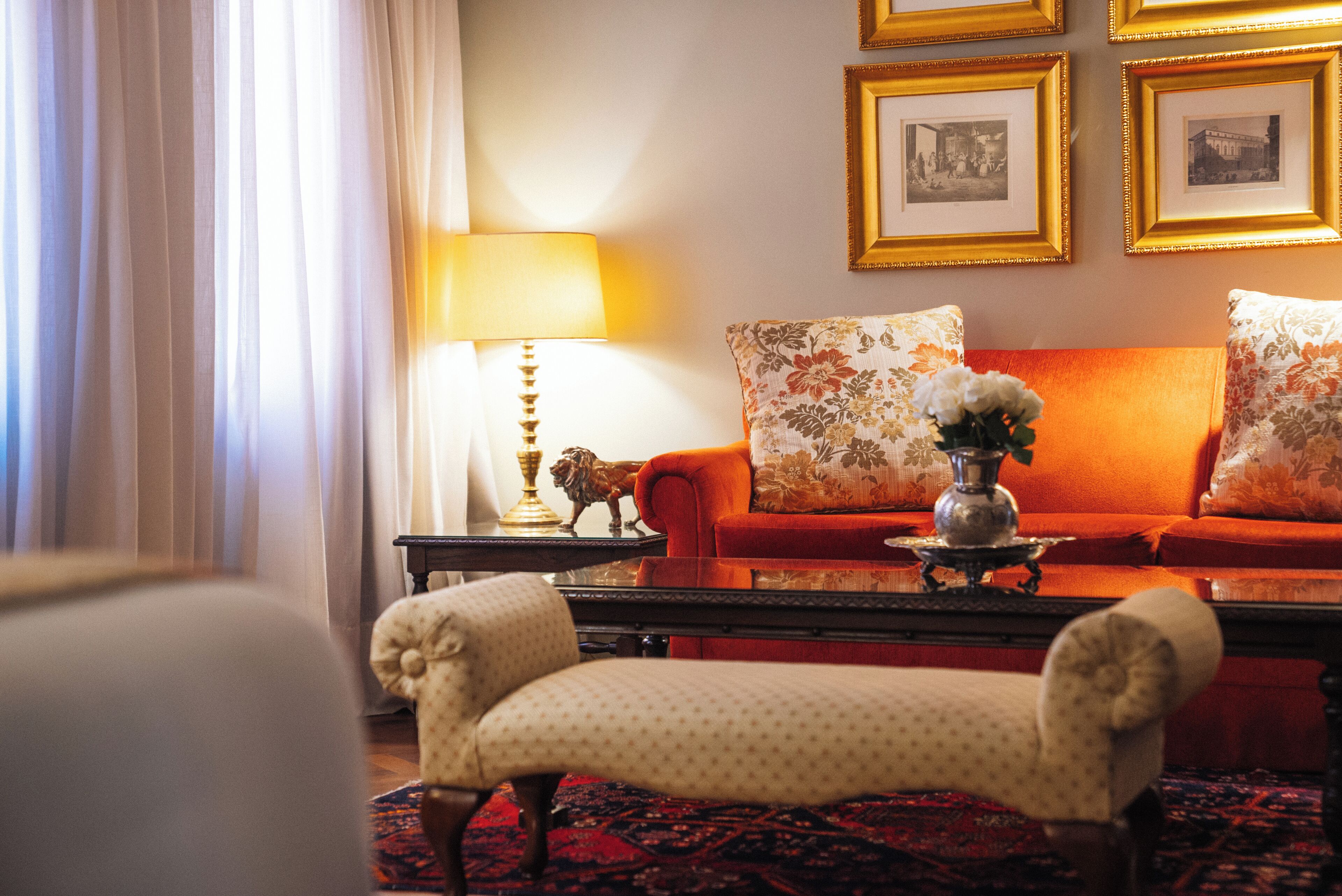 A room with a sofa, armchairs, a lamp, a table with a decorative item, and framed pictures on the wall.