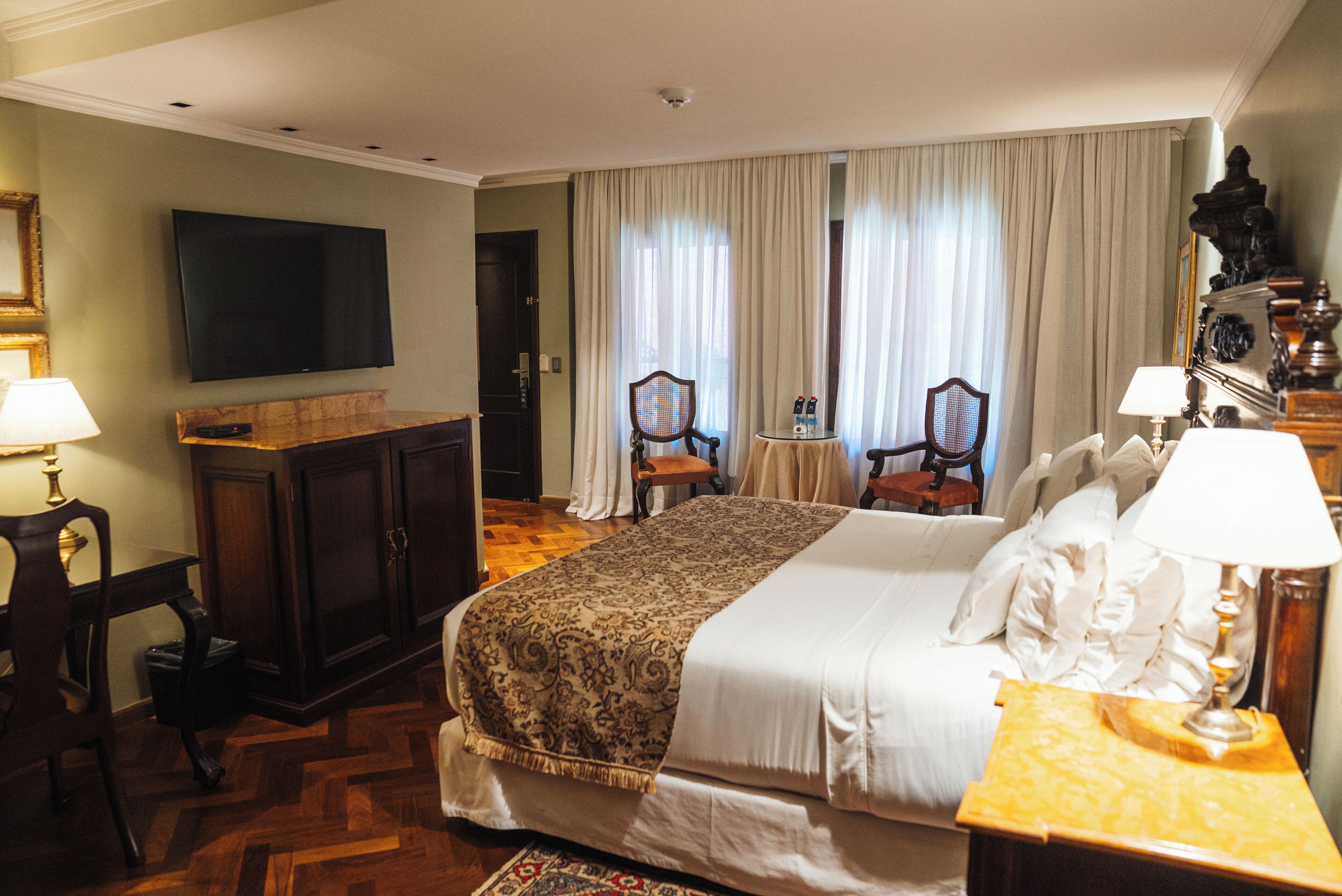 A hotel room with a bed, a television, a desk, and two chairs.