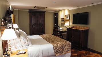 A hotel room with a bed, bedside table with lamps, a desk, a television, and a large wardrobe.