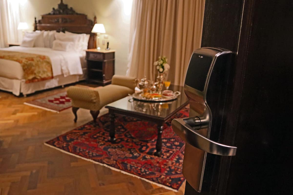 A hotel room with a bed, a sitting area with a table and chairs, a coffee table with a tray of items, and a door with a handle.