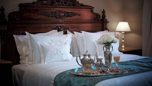 Ein ordentlich bezogenes Bett mit weißen Leinen und Kissen, ein Tablett mit Besteck und eine Vase mit weißen Blumen, sowie eine Lampe im Hintergrund.