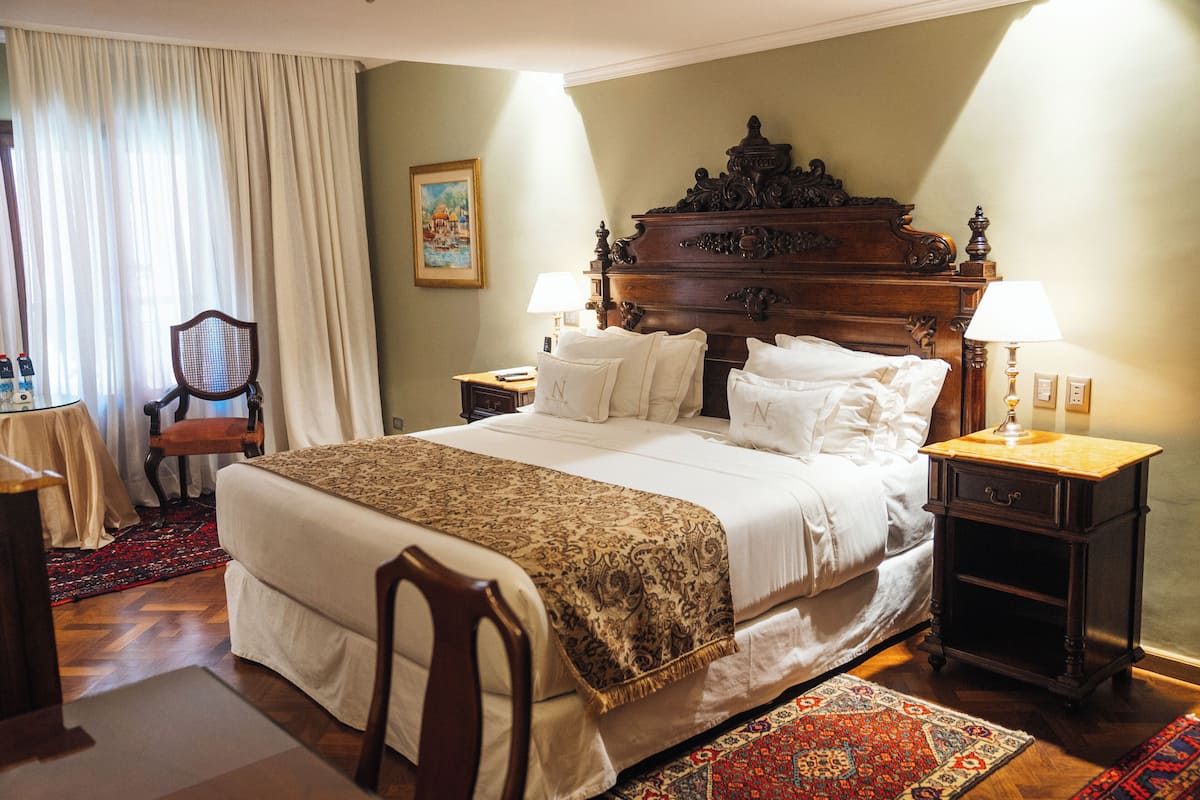 A hotel room with a large bed, two bedside tables, a chair, a desk, and a window with curtains.