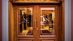 Eine imposante Holztür mit aufwendigen Schnitzereien und einem verspiegelten Glasspiegel, die zu einem gut beleuchteten Innenraum führt.