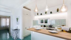 Uma cozinha moderna com armários brancos, bancada de madeira, luminárias pendentes e painel de azulejos.