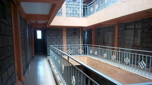A corridor with a metal railing, tiled floor, and a view of a building with a balcony. - Pinnacle Guest House (Mwingi)