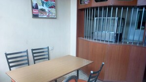 A dining area with a wooden table and two chairs, a poster on the wall, and a barred window. - Pinnacle Guest House (Mwingi)