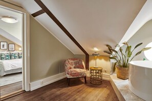 Un dormitorio con suelo de madera, un sillón floral, una mesita de noche y un ventanal grande.