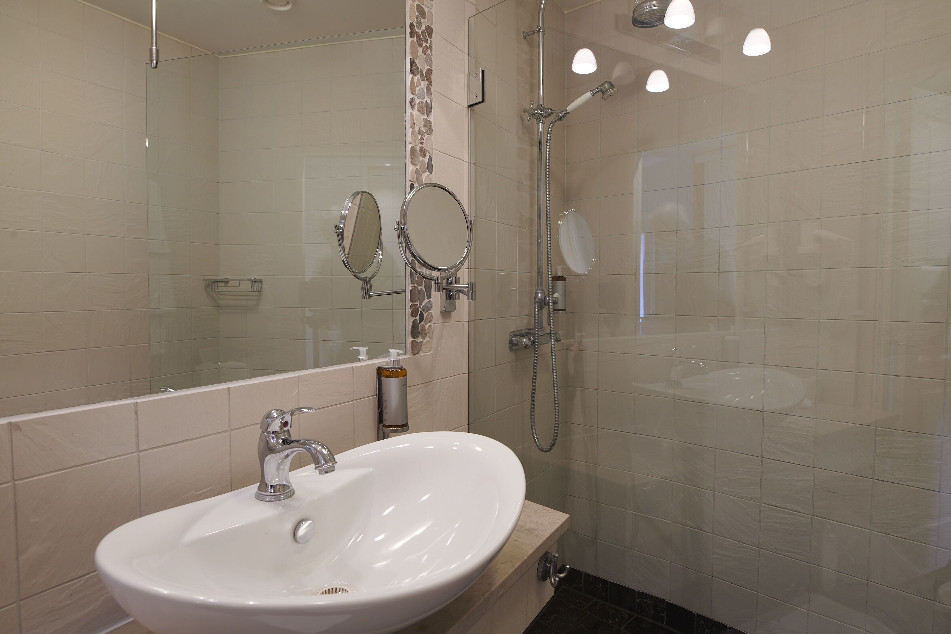 A bathroom with a white sink, two mirrors, a shower, and a glass-enclosed shower area.