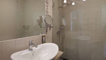 A bathroom with a white sink, two mirrors, a shower, and a glass-enclosed shower area.