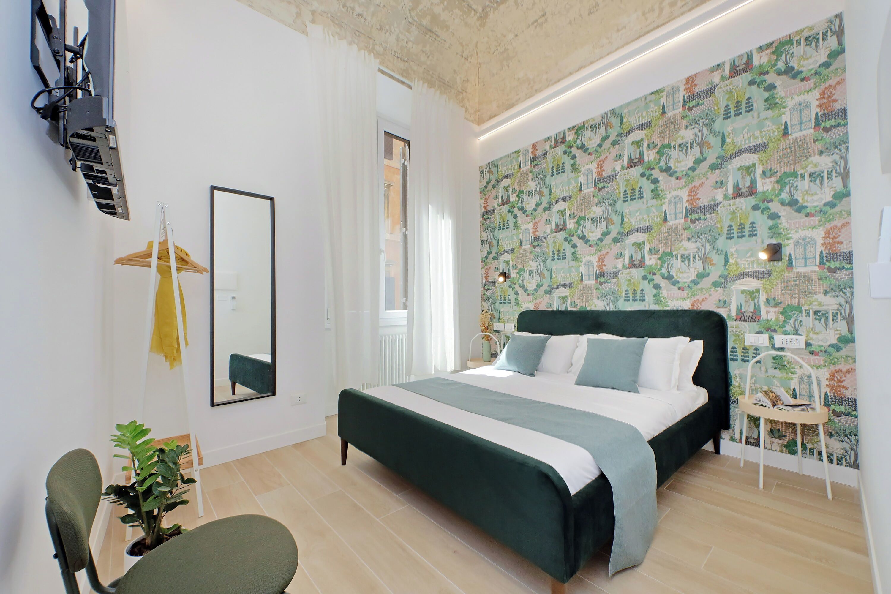 Ein modernes Schlafzimmer mit einem großen Bett, einem Spiegel, einer hängenden Pflanze und einer Wandtapete mit Muster.