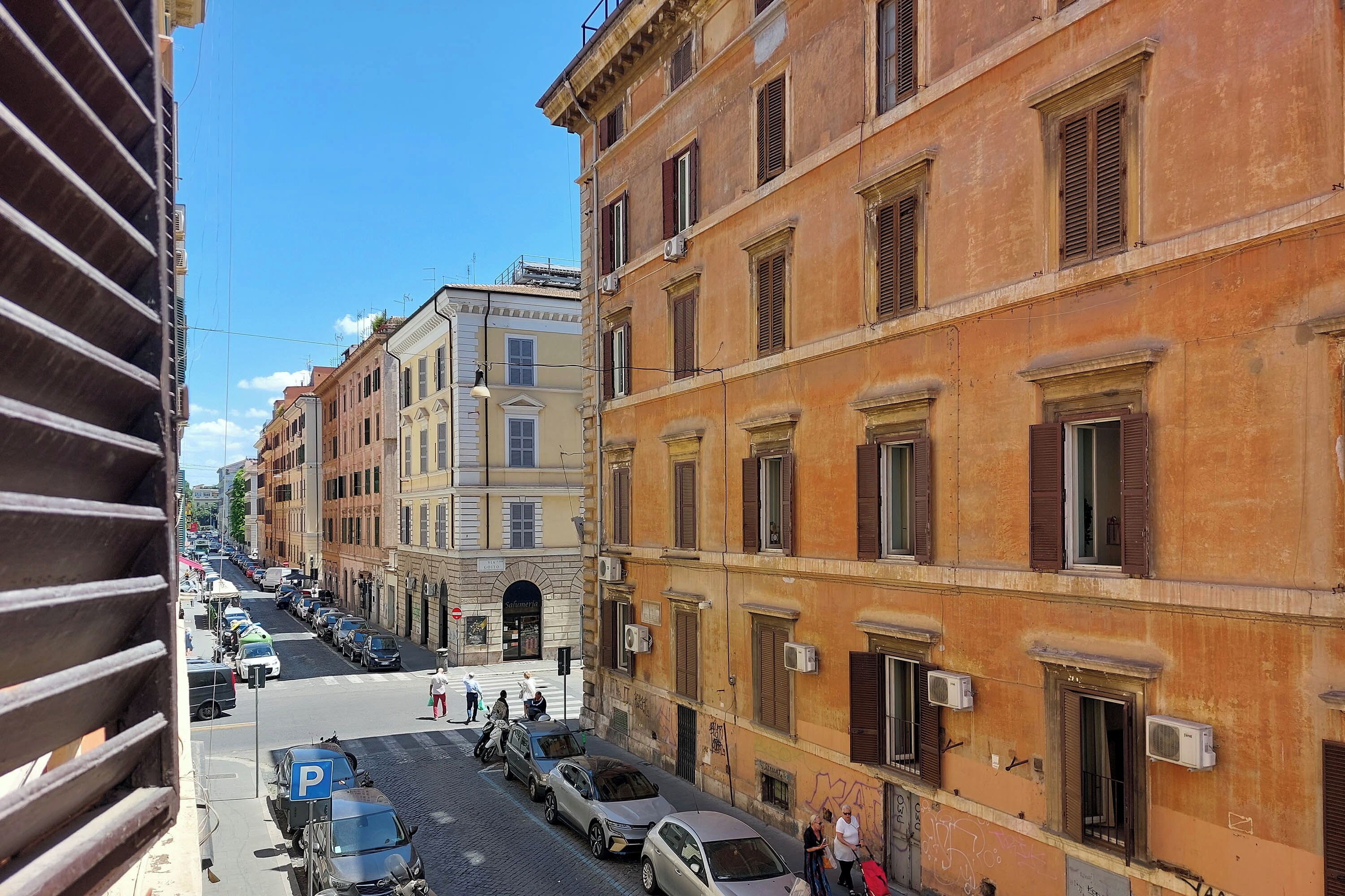 A street view with parked cars, buildings with brown shutters, and a clear blue sky.