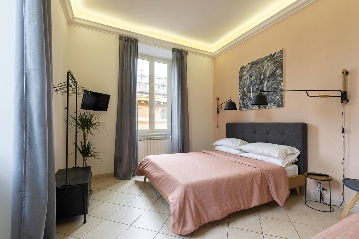 A bedroom with a bed, a TV, a painting, and a plant.