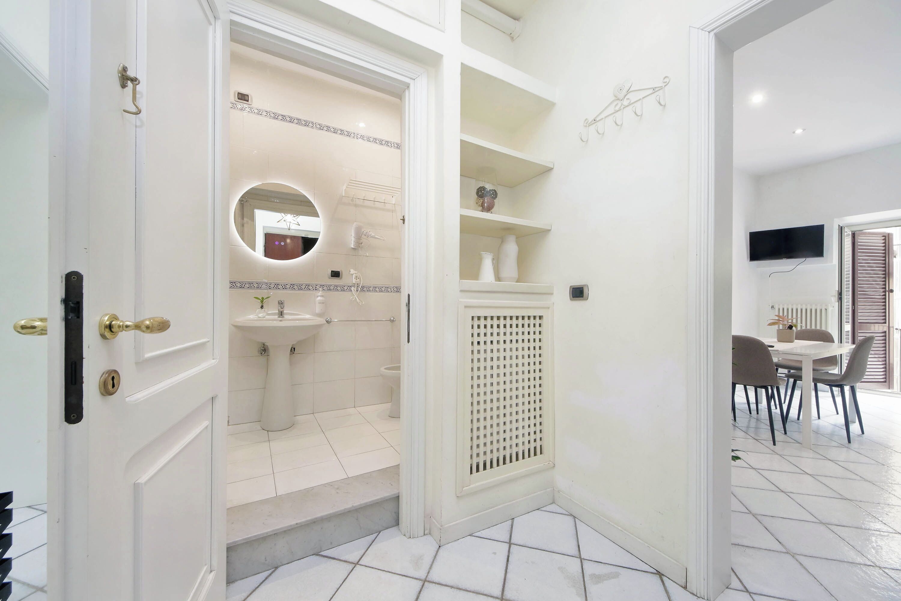 A modern bathroom with a sink, mirror, and toilet. There is a dining area with chairs and a table.