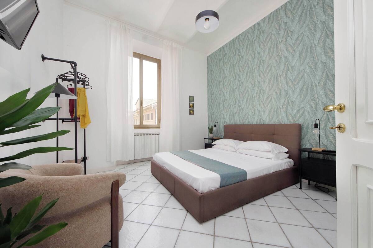 A bedroom with a bed, a chair, a radiator, a window, and a door.
