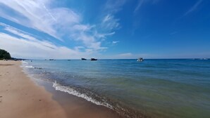 A beach with clear blue water, a sandy shore, and boats in the distance.