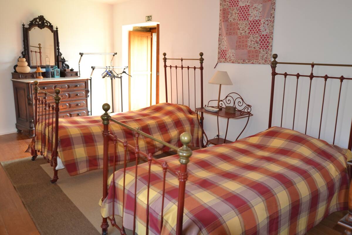 Une chambre avec deux lits, une commode, un miroir et une petite table avec une lampe.