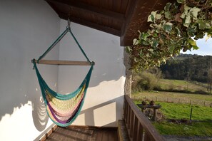 A hammock hanging on a balcony railing, overlooking a grassy landscape with a fence and trees.